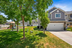 View of front of house with board and batten siding, a playground, concrete driveway, a garage, and stone siding