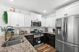 Kitchen featuring stainless steel appliances, white cabinets, recessed lighting,  wood-style flooring, and granite countertops