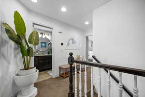 Corridor with an upstairs landing, recessed lighting, and light carpet