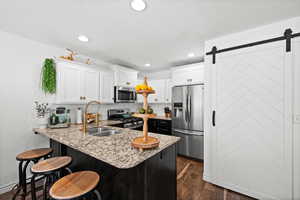 Kitchen with appliances with stainless steel finishes, a peninsula,  wood-style floors, white cabinetry, and a barn door