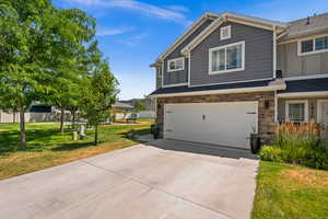 View of front facade with board and batten siding, a garage, stone siding, and driveway