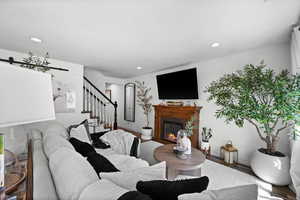 Living area featuring wood finished floors, recessed lighting, stairway, a glass covered fireplace, and a barn door