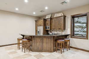 Kitchen featuring stainless steel microwave, refrigerator with ice dispenser, dark stone countertops, a kitchen breakfast bar, and recessed lighting