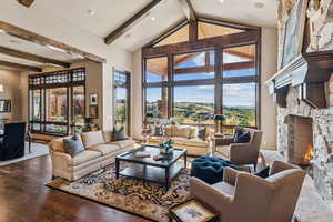 Living room with a fireplace, beamed ceiling, high vaulted ceiling, plenty of natural light, and wood finished floors