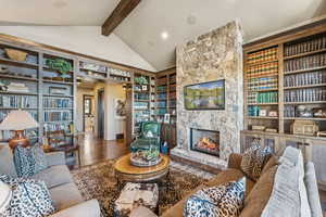 Living room featuring wood finished floors, a fireplace, beam ceiling, built in features, and high vaulted ceiling