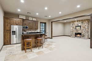 Kitchen with stainless steel appliances, recessed lighting, a kitchen bar, an island with sink, and dark stone countertops