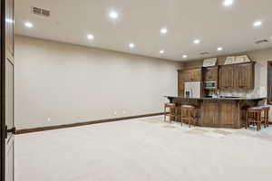 Kitchen with fridge with ice dispenser, stainless steel microwave, a breakfast bar, recessed lighting, and light carpet