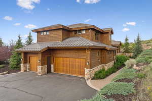 View of front of house featuring a standing seam roof, stone siding, a metal roof, and driveway