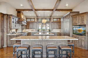 Kitchen featuring glass insert cabinets, dark wood-type flooring, beam ceiling, decorative backsplash, and a breakfast bar area