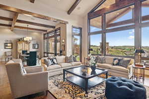 Living room featuring beamed ceiling, a chandelier, dark wood-style flooring, and a towering ceiling