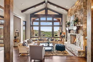 Living area featuring high vaulted ceiling, beam ceiling, wood finished floors, and a stone fireplace