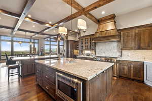 Kitchen with light stone countertops, decorative backsplash, coffered ceiling, beam ceiling, and hanging light fixtures