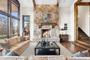 Living area with a fireplace, beamed ceiling, wood finished floors, stairs, and a towering ceiling