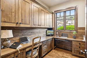 Office space with built in study area, light wood finished floors, and wooden walls