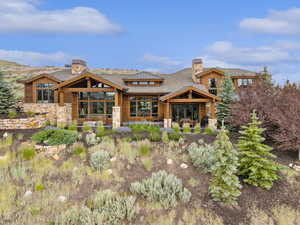 Back of property featuring a chimney, a patio, stone siding, and a shingled roof