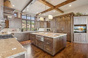 Kitchen featuring a warming drawer, an island with sink, dark wood-type flooring, decorative backsplash, and beam ceiling