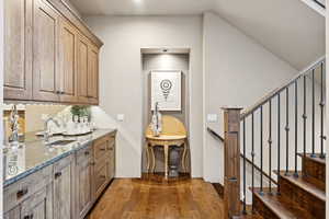 Bar with dark stone counters, dark wood-style floors, brown cabinetry, and stairs