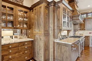 Kitchen featuring stainless steel stove, glass insert cabinets, light stone counters, and dark wood-style floors