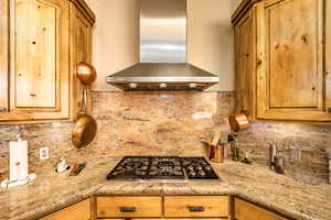 Kitchen featuring island range hood, stainless steel gas stovetop, backsplash, and light stone counters