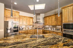 Kitchen featuring appliances with stainless steel finishes, wall chimney range hood, a skylight, and decorative backsplash