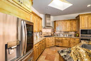 Kitchen featuring stainless steel appliances, wall chimney range hood, a skylight, backsplash, and recessed lighting
