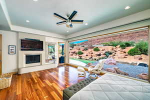 Bedroom featuring access to outside, wood finished floors, a glass covered fireplace, recessed lighting, and ceiling fan