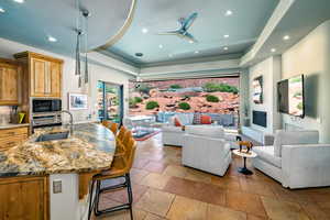 Living room with a tray ceiling, a ceiling fan, recessed lighting, and stone finish flooring