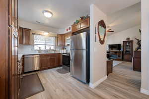 Kitchen featuring appliances with stainless steel finishes, light wood finished floors, brown cabinetry, decorative backsplash, and a textured ceiling