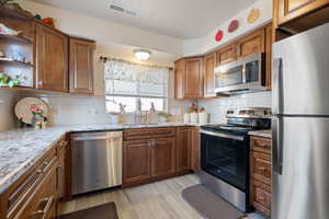 Kitchen with appliances with stainless steel finishes, open shelves, light wood finished floors, light stone counters, and decorative backsplash
