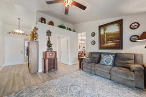 Living area featuring light wood-style floors, a chandelier, and a ceiling fan