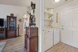 Laundry room with washer and clothes dryer and light wood-style flooring
