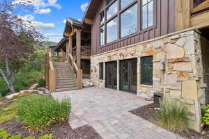 Rear view of house with stone siding, board and batten siding, stairway, and a patio