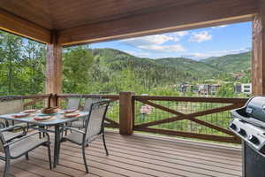 Wooden deck featuring a mountain view, outdoor dining area, grilling area, and a wooded view