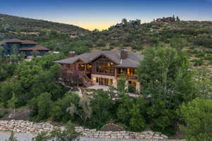 Back of property at dusk featuring stone siding, stairs, and a chimney