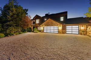 View of front of home featuring stone siding, decorative driveway, an attached garage, and a chimney