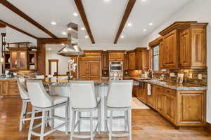 Kitchen with extractor fan, beamed ceiling, backsplash, a kitchen bar, and brown cabinetry