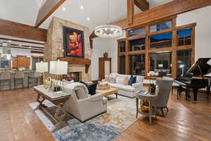 Living area featuring high vaulted ceiling, beam ceiling, hardwood / wood-style floors, a fireplace, and a chandelier