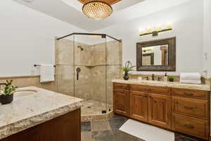 Bathroom featuring two vanities, a stall shower, tile walls, and a wainscoted wall