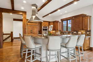 Kitchen with island exhaust hood, beam ceiling, backsplash, stainless steel oven, and light wood-style floors