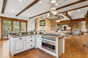 Kitchen with island range hood, beamed ceiling, white cabinets, appliances with stainless steel finishes, and wood finished floors