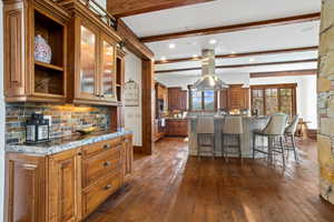 Kitchen featuring dark wood finished floors, a breakfast bar area, brown cabinetry, tasteful backsplash, and beam ceiling