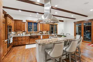 Kitchen with island range hood, oven, beamed ceiling, brown cabinets, and backsplash
