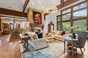 Living room featuring beamed ceiling, a towering ceiling, wood-type flooring, a chandelier, and a fireplace
