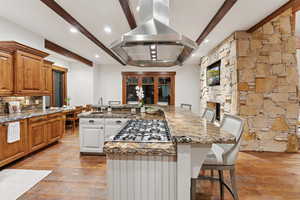 Kitchen featuring island exhaust hood, stainless steel gas stovetop, beamed ceiling, light wood finished floors, and a large island