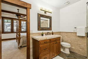 Bathroom with a ceiling fan, vanity, tile walls, wainscoting, and ensuite bathroom
