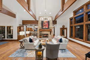 Living area with high vaulted ceiling, a chandelier, beamed ceiling, a stone fireplace, and wood finished floors