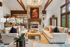 Living room with high vaulted ceiling, beamed ceiling, a chandelier, a stone fireplace, and wood finished floors