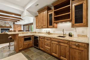 Kitchen with wine cooler, stainless steel microwave, a breakfast bar area, a peninsula, and brown cabinetry