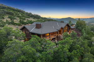 Back of house at dusk with a shingled roof, a mountain view, board and batten siding, a chimney, and covered porch