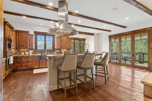 Kitchen featuring island range hood, oven, brown cabinetry, beam ceiling, and recessed lighting